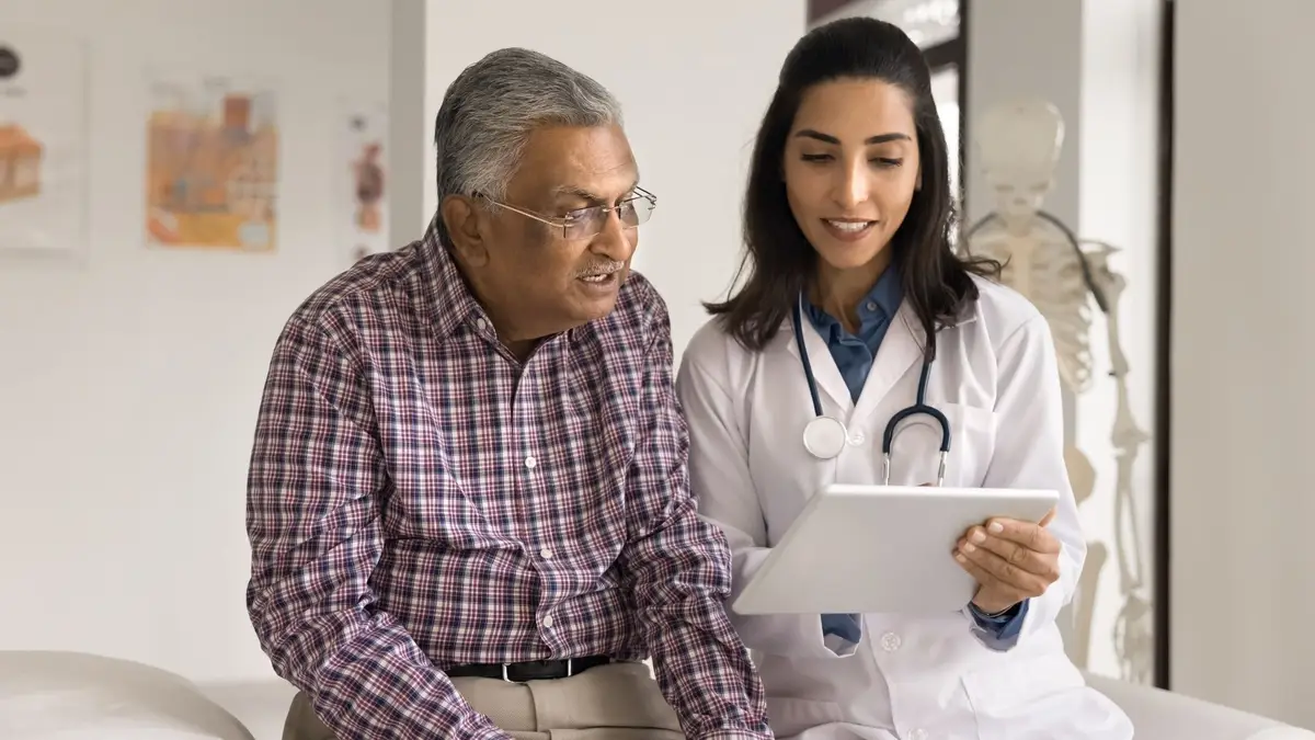 Doctor discussing medical information with a senior patient during a consultation, reviewing details on a digital tablet in a healthcare clinic. The image highlights health insurance planning, preventive healthcare, medical guidance, senior citizen health coverage, and informed healthcare decisions.